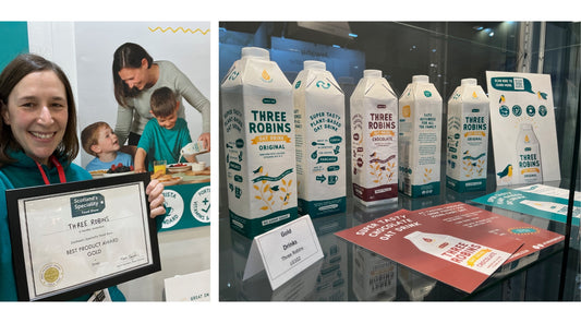 Three Robins founder, Karen Robinson, holds gold certificate. Cartons of Three Robins oat milk in display case