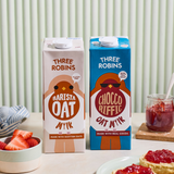 Three Robins Barista and Choccoriffic oat milk cartons beside bowl of cut strawberries and scone with jam