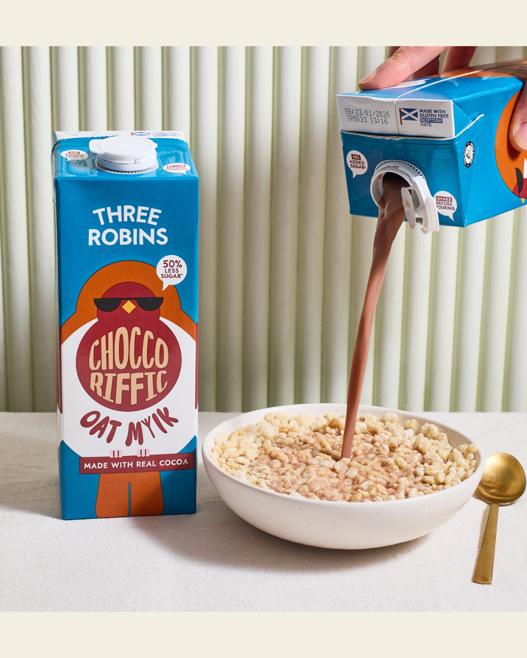 Three Robins Choccoriffic oat milk carton beside bowl of cereal with chocolate mil being poured in