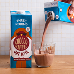 Three Robins Choccoriffic oat milk carton beside glass of chocolate milk being poured
