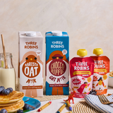 Busy family breakfast table with Three Robins Barista and Choccoriffic oat milk cartons and Three Robins Super Berry and Totally Tropical Little Smoothie pouches