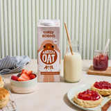 Three Robins Barista oat milk on table with strawberries, glass of oat milk with straw, scone with jam and jam jar