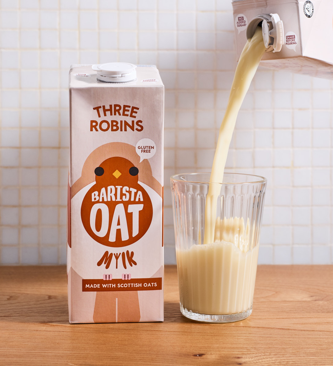 Three Robins Barista oat milk carton beside a glass of oat milk being poured