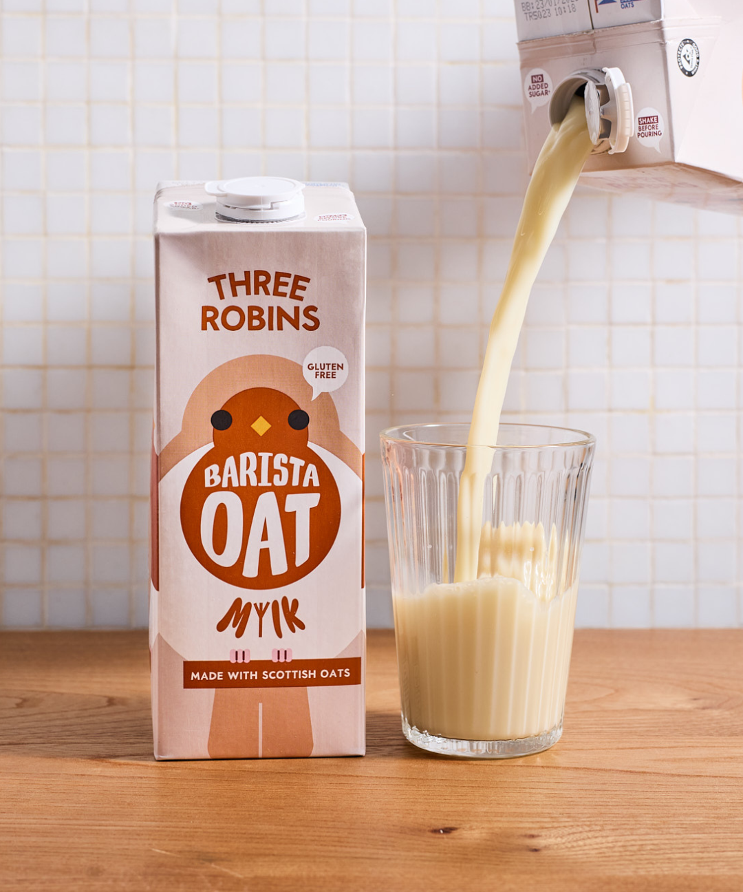 Three Robins Barista oat milk carton beside a glass of oat milk being poured