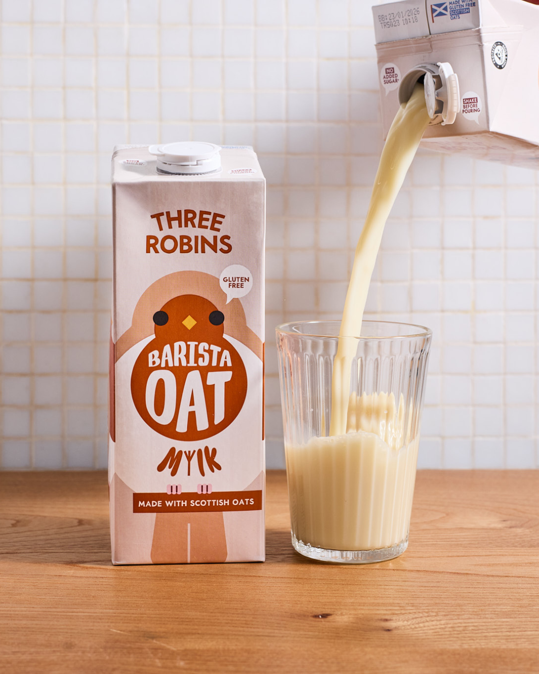 Three Robins Barista oat milk carton beside a glass of oat milk being poured