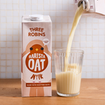 Three Robins Barista oat milk carton beside a glass of oat milk being poured