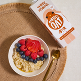 Three Robins Barista oat milk carton laying flat beside bowl of porridge with fruit and golden syrup on top