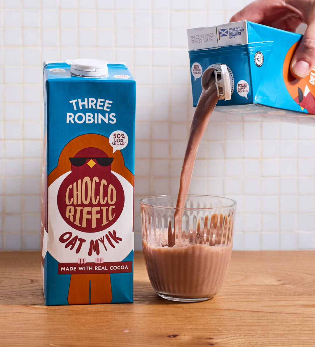 Three Robins Choccoriffic oat milk carton beside glass of chocolate milk being poured