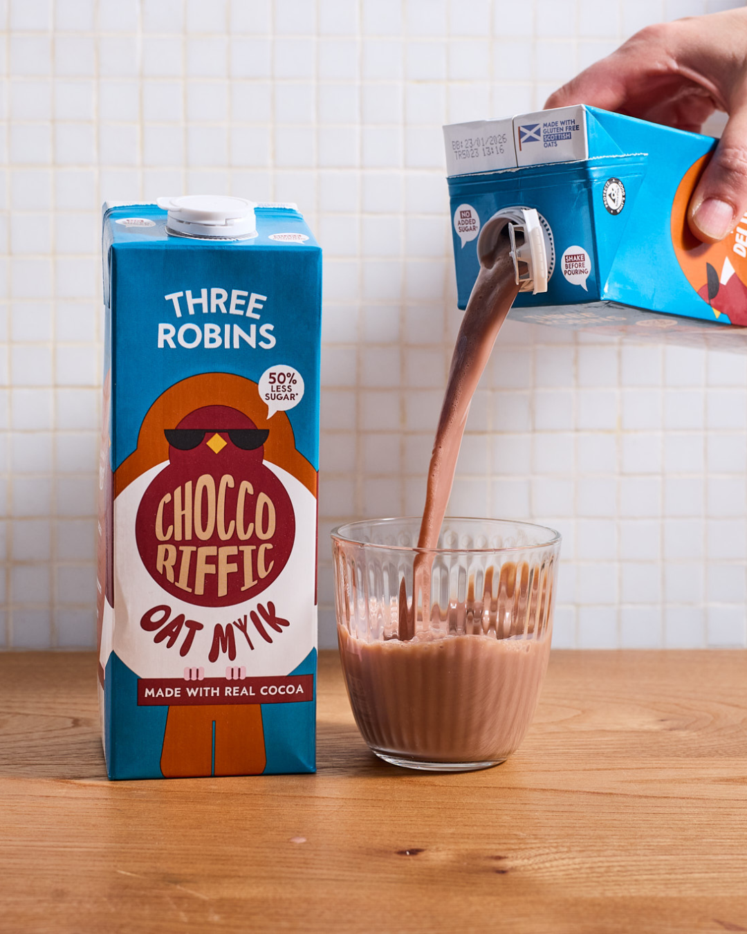 Three Robins Choccoriffic oat milk carton beside glass of chocolate milk being poured