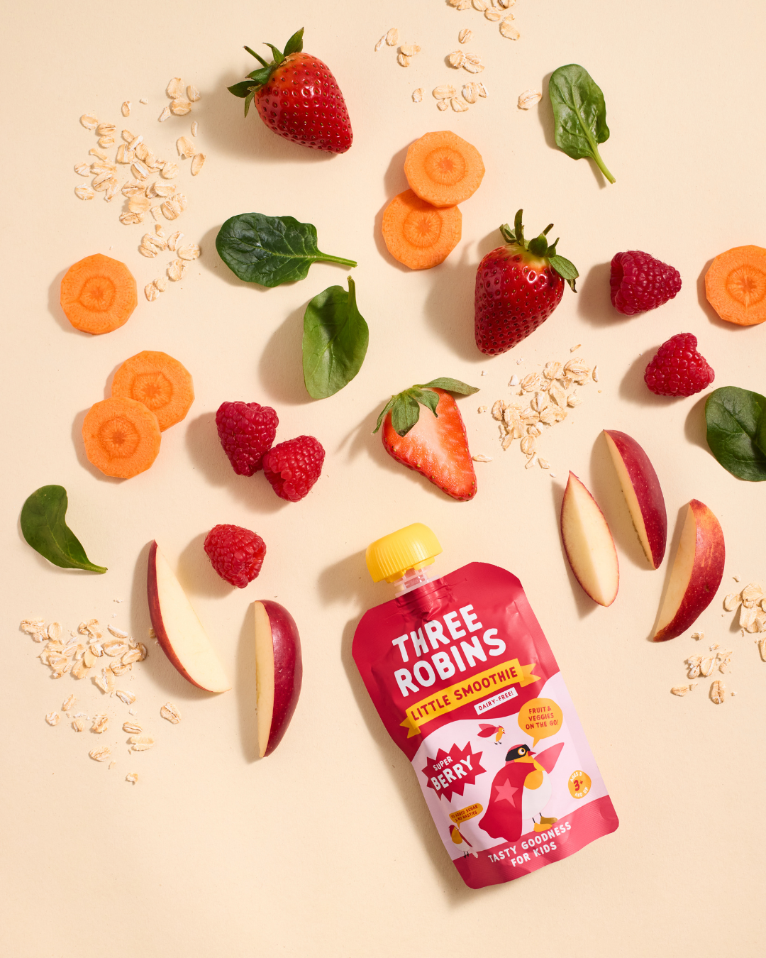 Three Robins Super Berry Little Smoothie pouch surrounded by fruit and veg including apple, raspberry, carrot, spinach and strawberries and oats