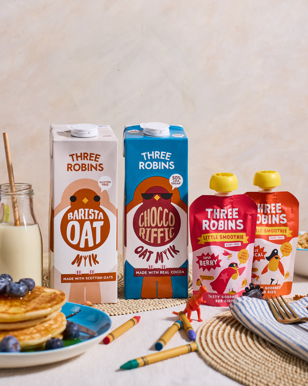 Busy family breakfast table with Three Robins Barista and Choccoriffic oat milk cartons and Three Robins Super Berry and Totally Tropical Little Smoothie pouches 