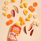 Three Robins Totally Tropical Little Smoothie pouch surrounded by cut fruit and veg including carrots, apples, bananas, oranges and mangoes