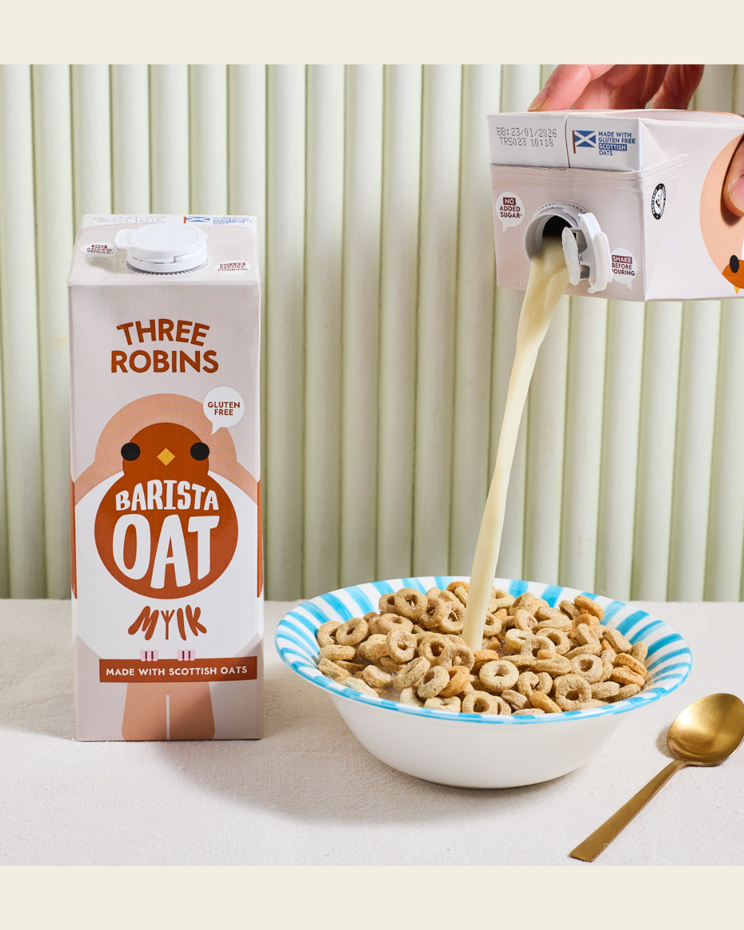 Three Robins barista oat milk carton beside a bowl of cereal with oat milk being poured in 